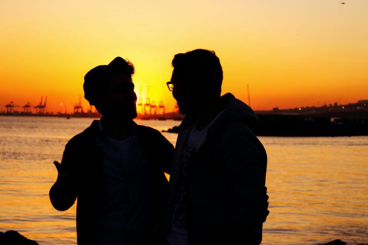 a couple of men as a silhouette with sunset behind them near the sea