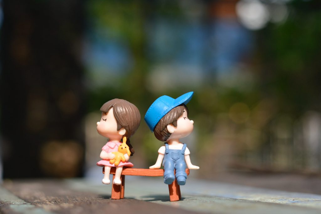 toy boy and girl, sitting on a bench, facing opposite direction