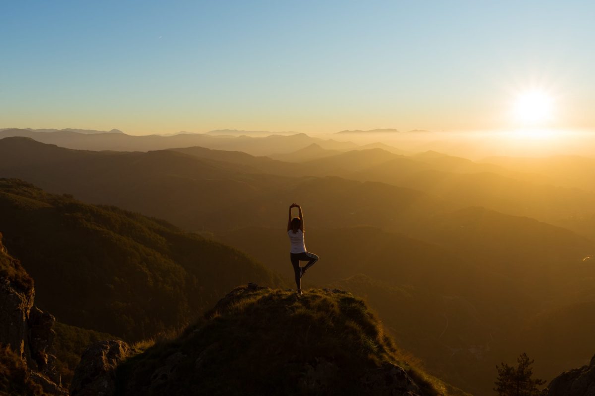 woman in yoga pose atop a mountain during sunset
