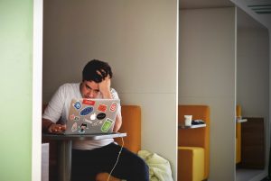 man sitting at a desk, with a latop, looking frustrated