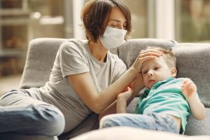mother checking childs head for temperature whilst wearing surgical mask