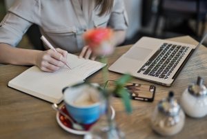 persona writing on a notebook beside a laptop