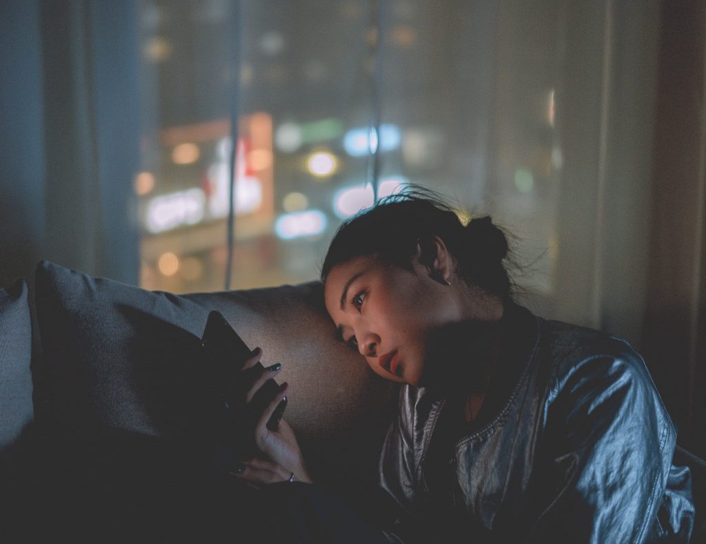 woman on sofa, staring at mobile phone at night time.