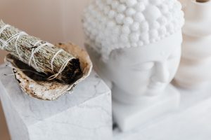 sage smmudge stick in a bowl on a marble shelf next to buddha head