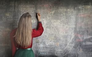 Woman writing complex equations on a blackboard.